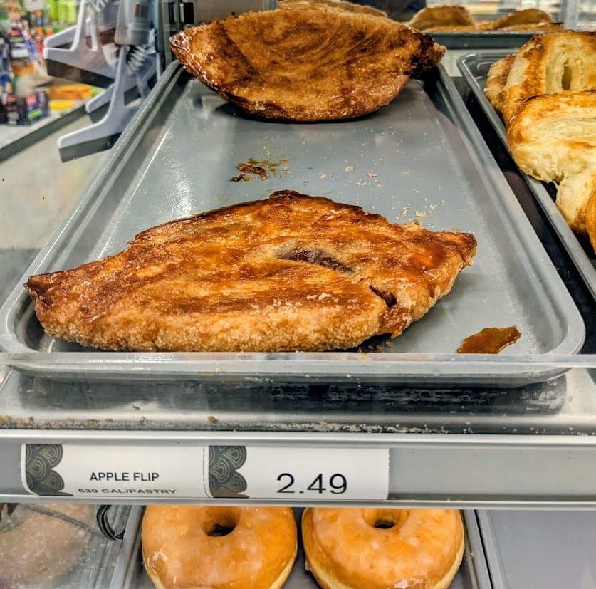 A shelf inside a grab-and-go Publix Bakery case with a tray of Apple Flip pastries. The sign lists the calories as 530 per pastry.