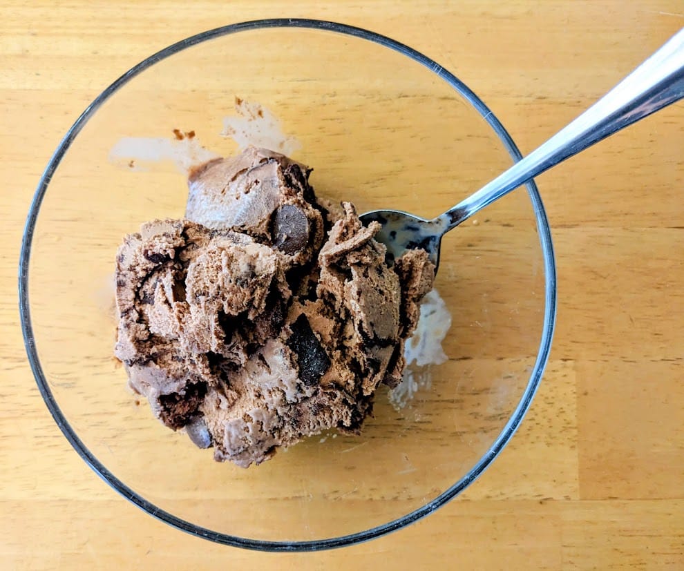 A clear glass bowl of Publix Chocolate Moose Tracks Ice Cream with a spoon on a kitchen table.