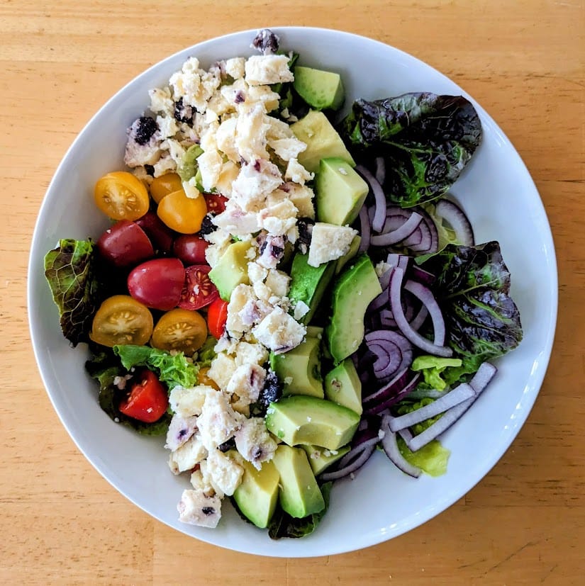 A white bowl with a salad topped with crumbles of Somerdale Wensleydale & Blueberries cheese.