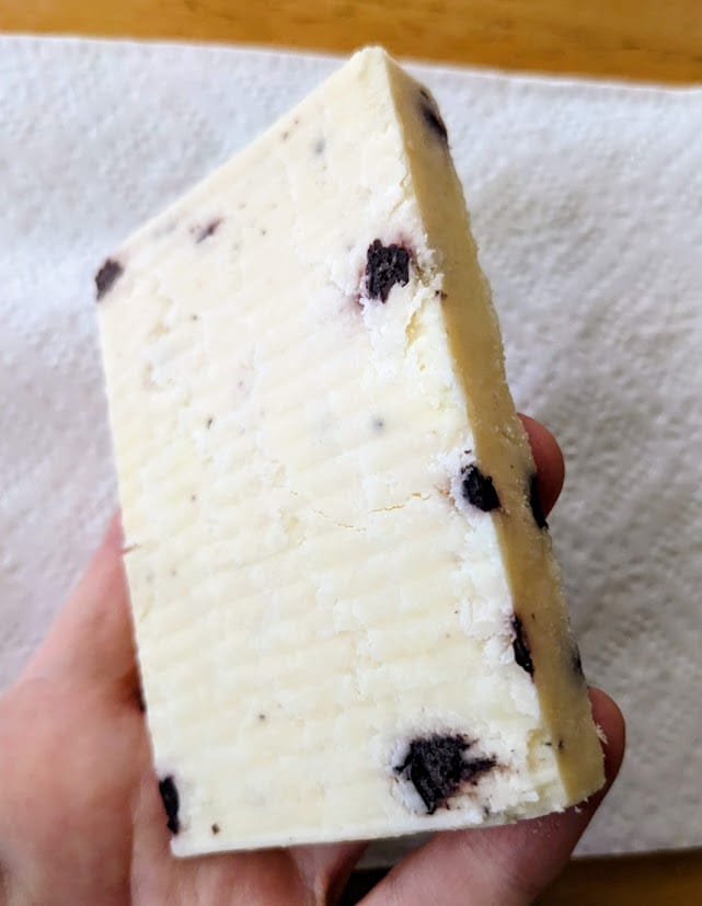A hand holding a thick slice of Somerdale blueberry flavored Wensleydale cheese from Costco.
