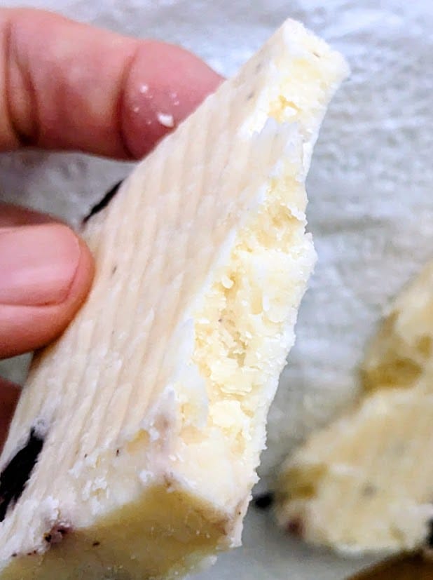 Fingers holding a fragment of Wensleydale & Blueberries cheese from Somerdale brand.
