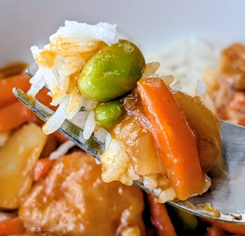 A fork with carrots and edamame from a PF Chang's Orange Chicken frozen meal.