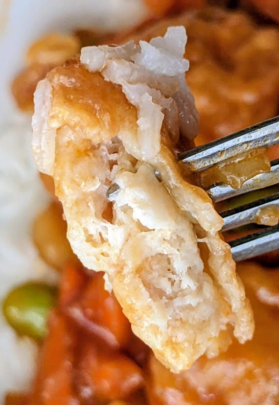 A fork holding a bite of meat from a PF Chang's frozen Orange Chicken meal.