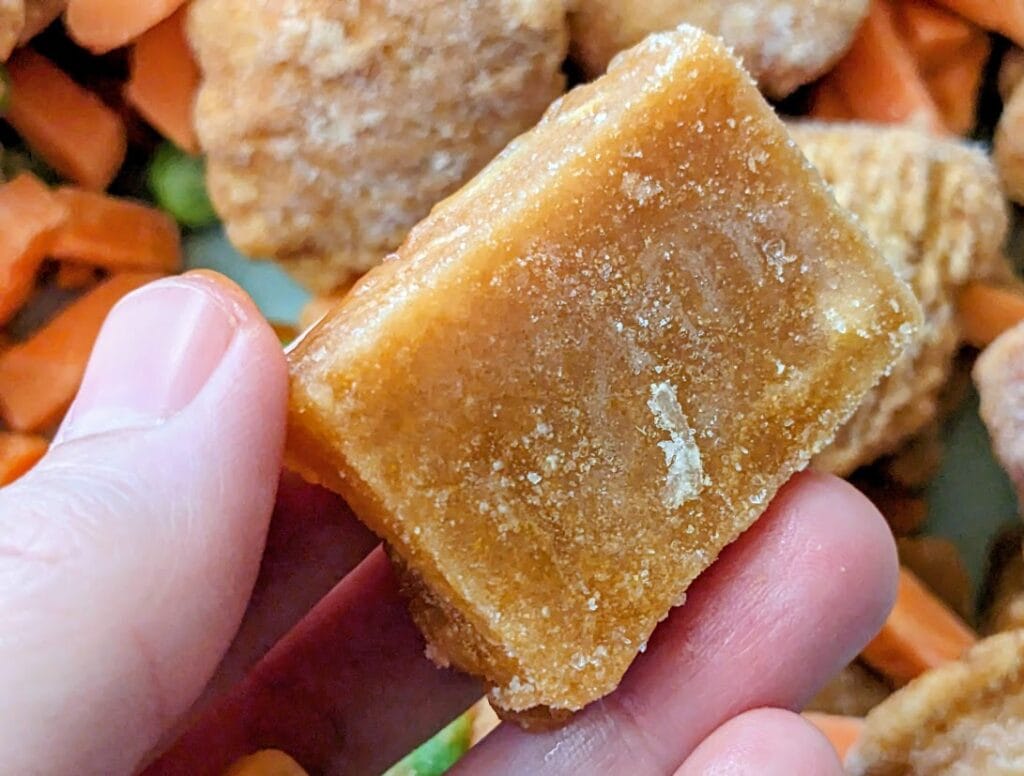 Fingers holding a frozen cube of PF Chang's Orange Chicken sauce.
