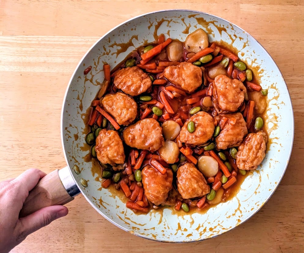 A hand holding a skillet with a cooked PF Chang's Orange Chicken frozen meal.