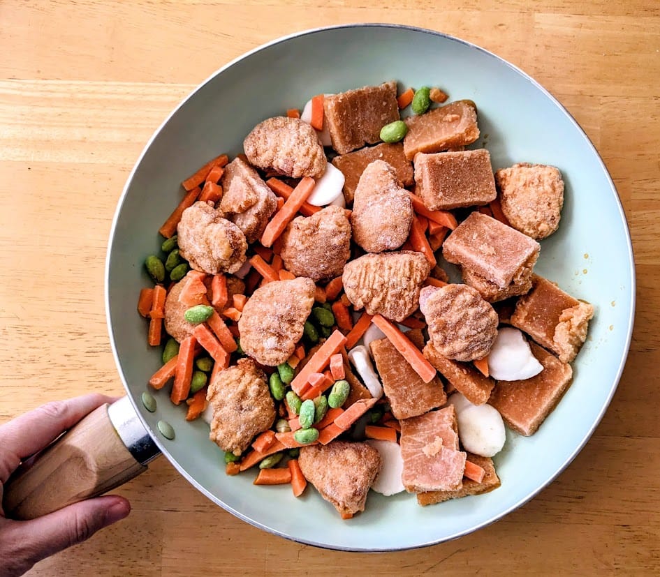 A hand holding a skilled with the contents of a PF Chang's frozen Orange Chicken meal.