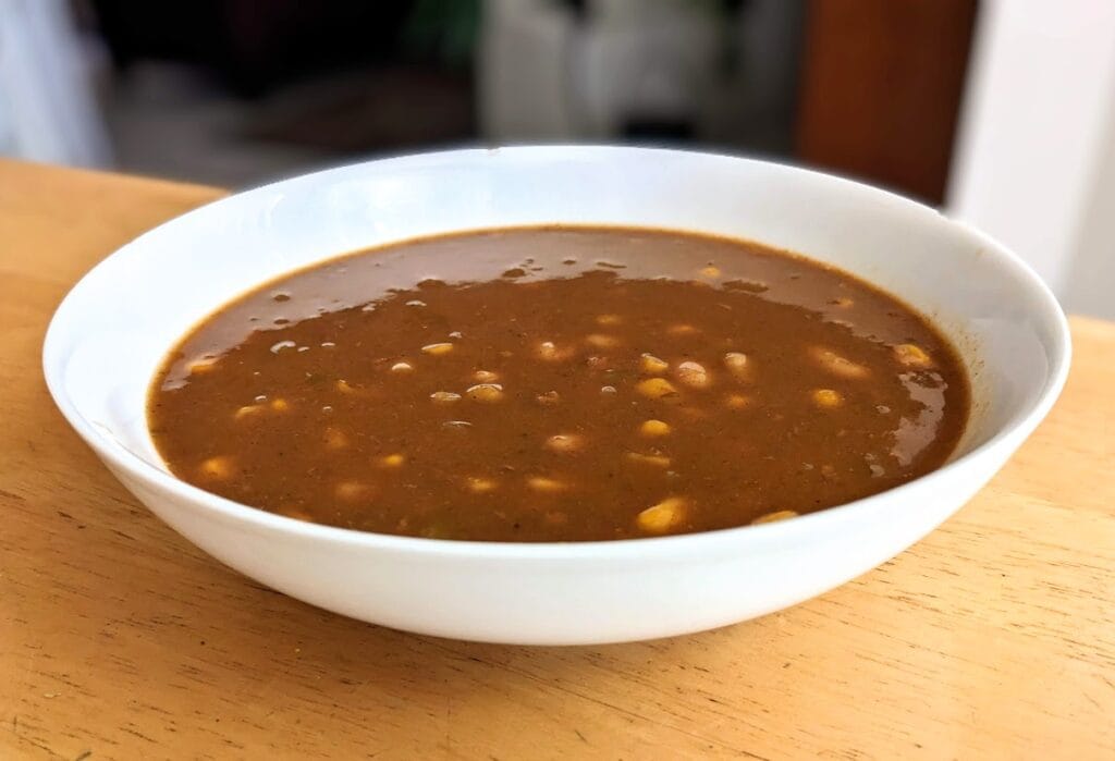 Side view of a bowl of Zoup White Chicken Chili soup sitting on a kitchen table.