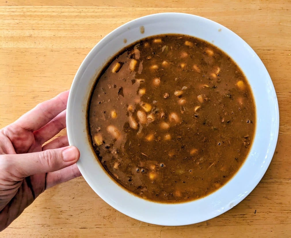 A hand holding a bowl filled with Zoup! White Chicken Chili soup.