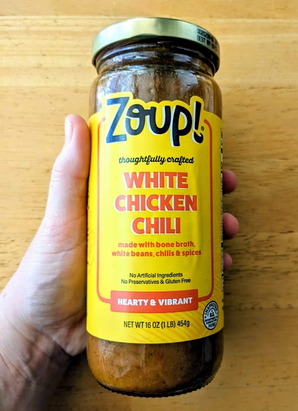 A hand holding a jar of Zoup! White Chicken Chili soup.