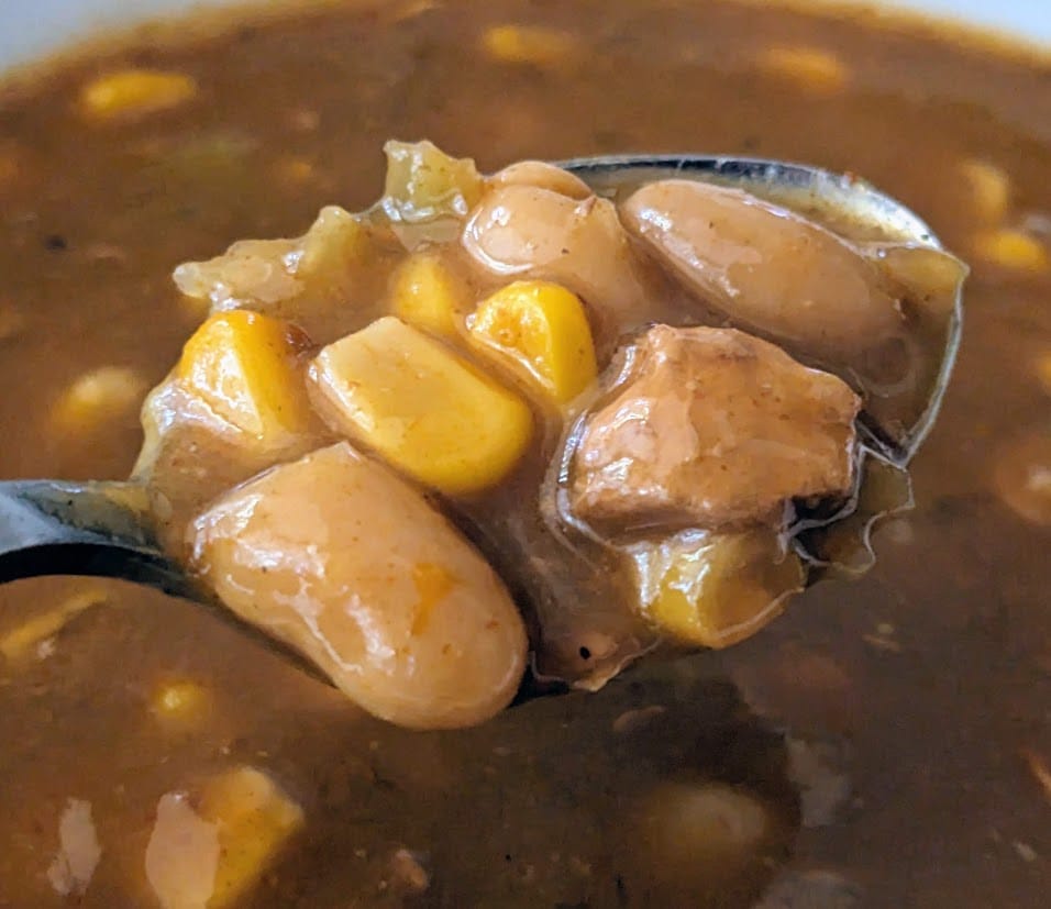 A spoonful of Zoup White Chicken Chili soup, showing beans, corn, and meat.