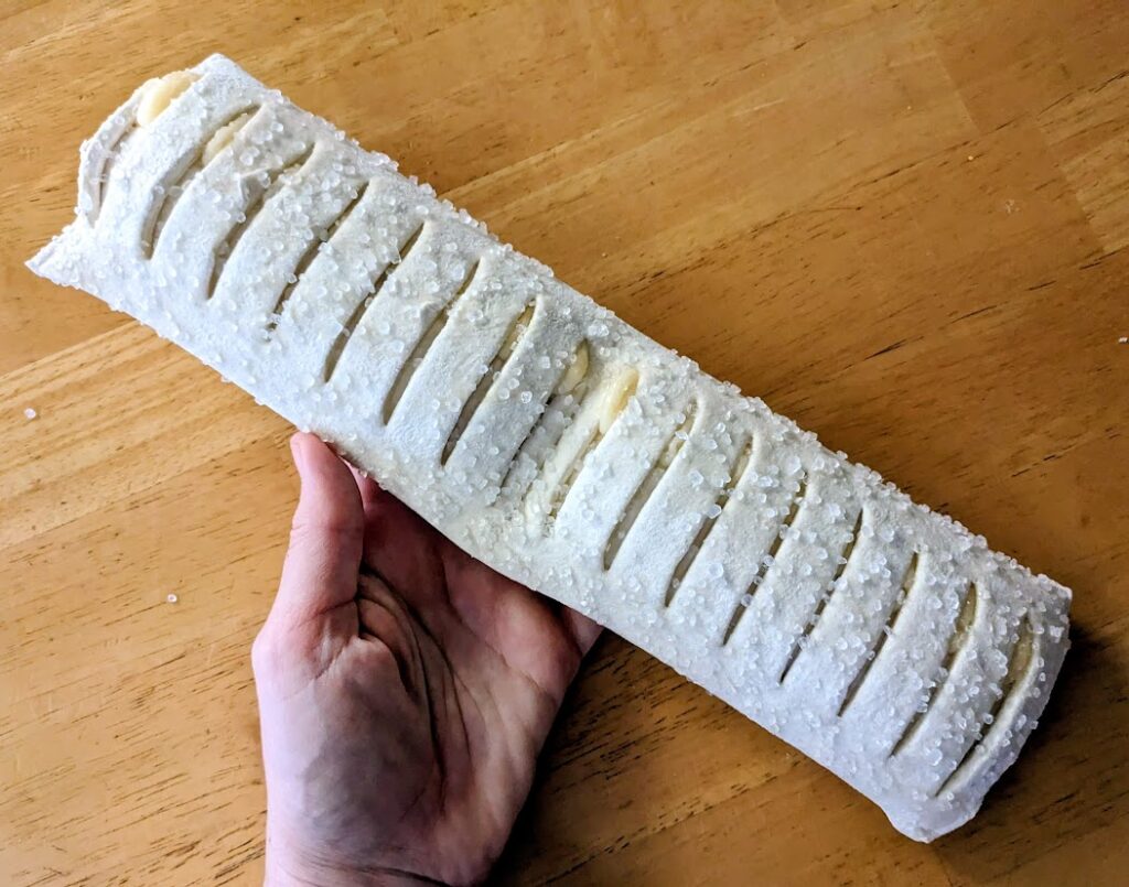 A hand holding a whole frozen, raw Lemon Mascarpone strudel from Aldi.