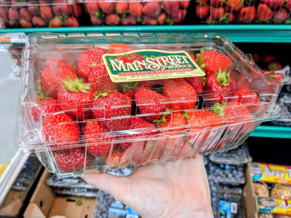 A hand holding a plastic box of Mainstreet brand strawberries inside a BJ's Wholesale Club.