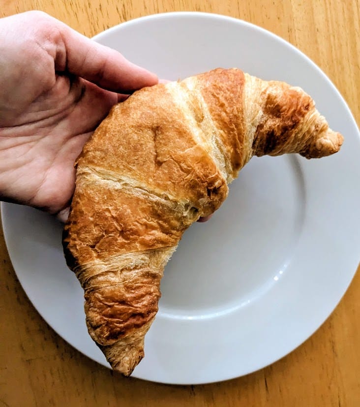 A hand holding a croissant from BJ's Wholesale Club.