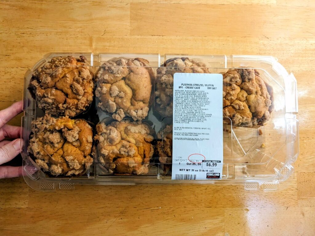 A hand holding a box of Costco Bakery Pumpkin Streusel Muffins.