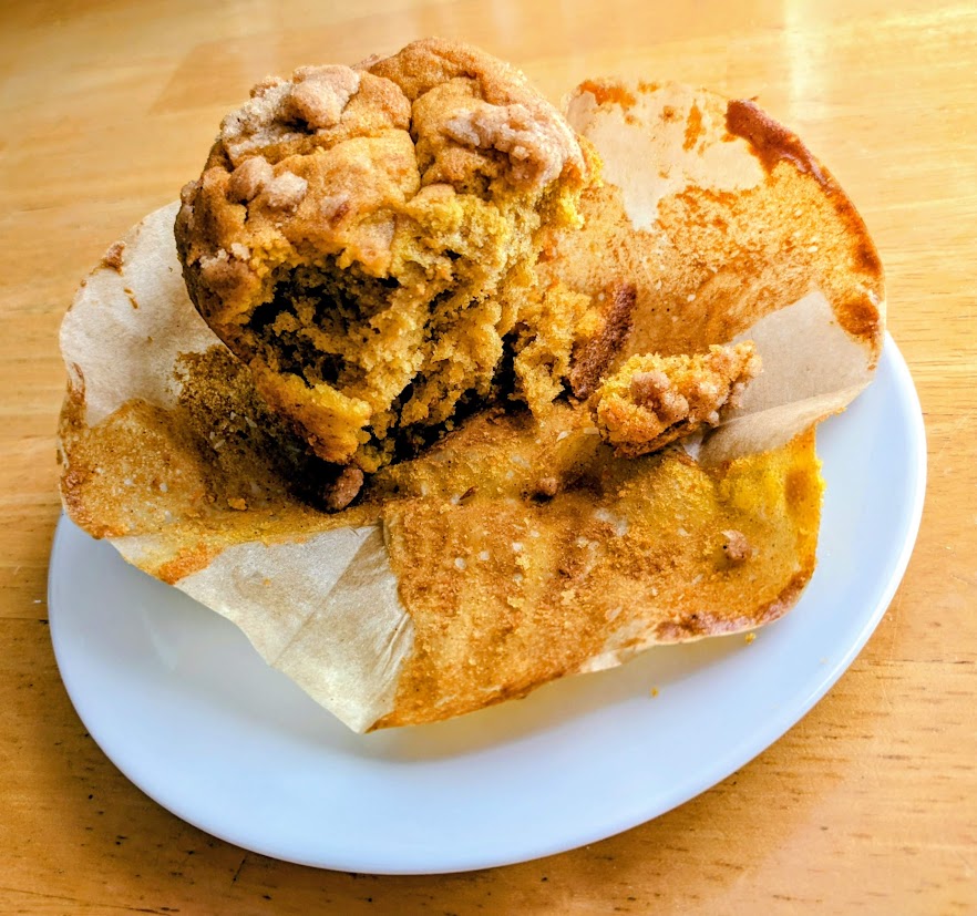 Half-eaten Costco Pumpkin Streusel Muffin, sitting on a white plate.