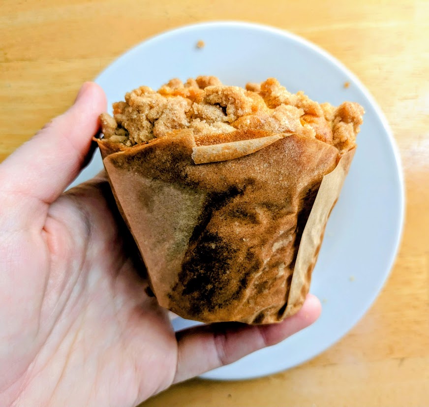 A hand holding a whole Costco Pumpkin Streusel Muffin over a white plate.