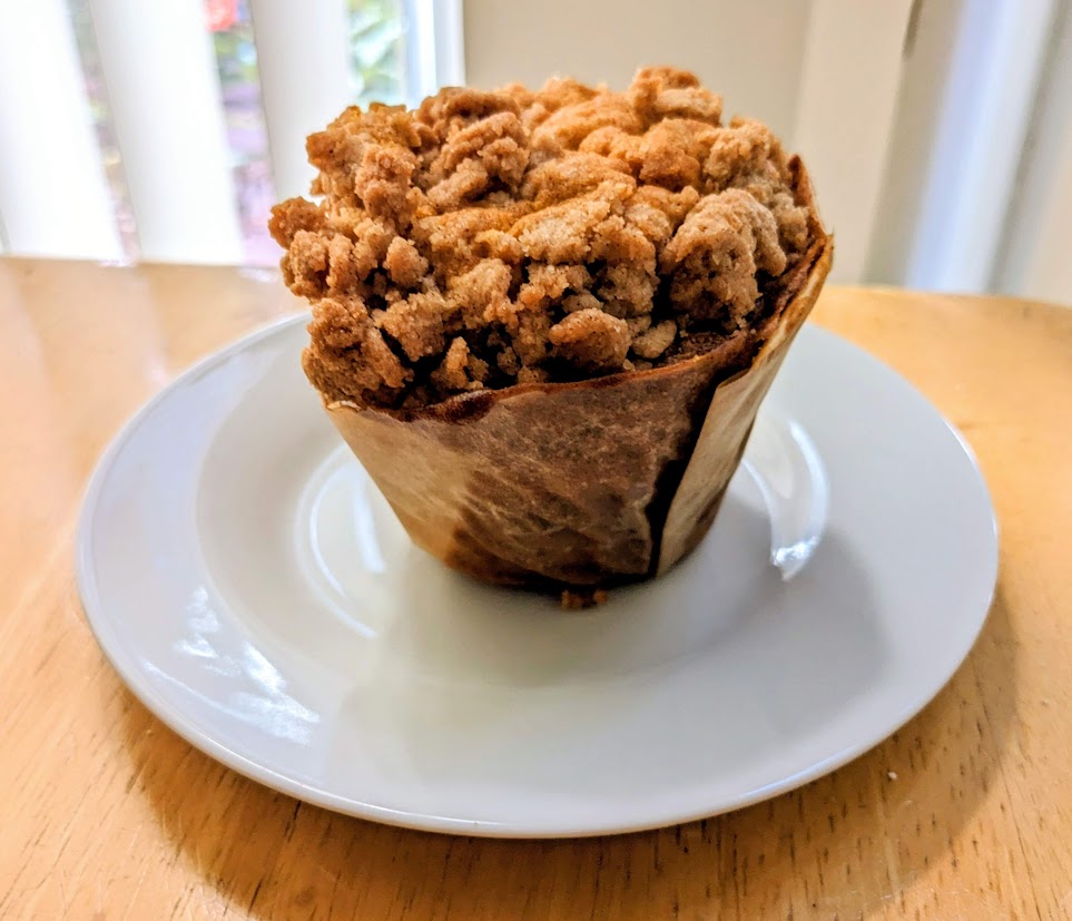 A whole paper-wrapped Pumpkin Streusel Muffin from the Costco Bakery, sitting on a white plate.