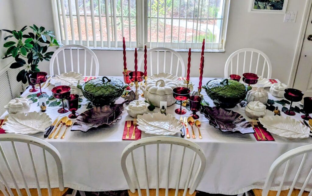 A long dinner table set with holiday dishware in front of a window.