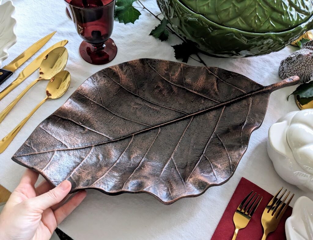 A hand holding a bronze metal leaf tray on a holiday dinner table.