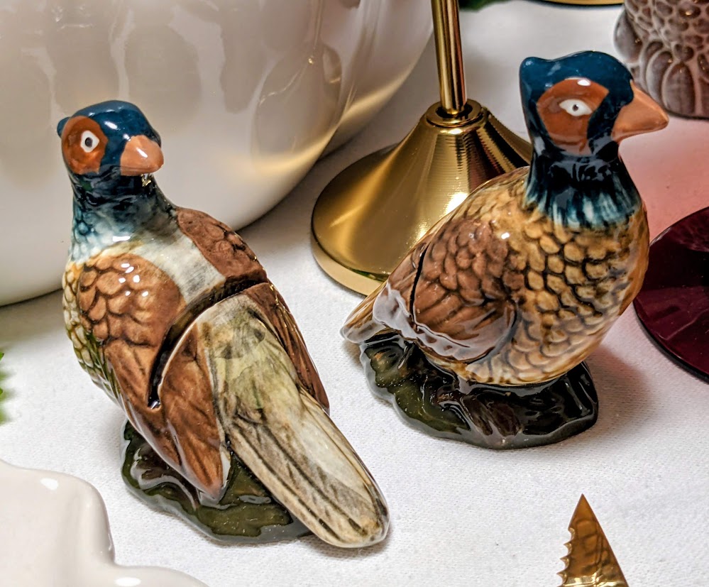 Two ceramic pheasant name card holders on a holiday dinner table.